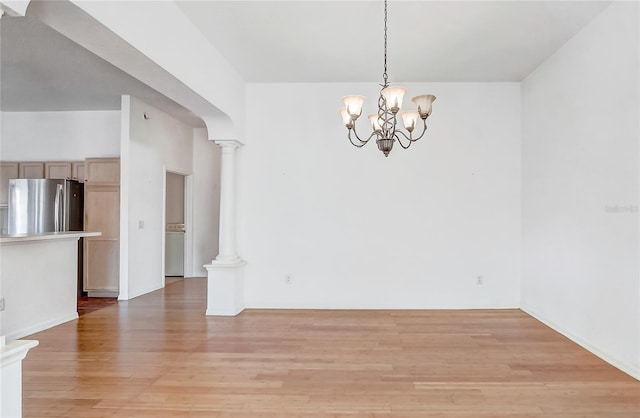 unfurnished dining area with ornate columns, light wood-style flooring, arched walkways, and a notable chandelier