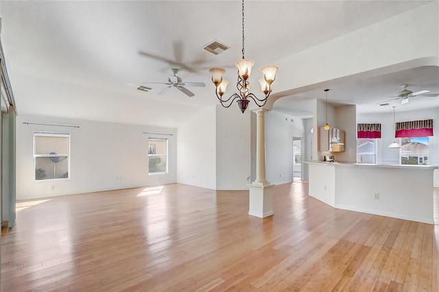 unfurnished living room featuring ceiling fan with notable chandelier, light wood-style flooring, visible vents, and ornate columns