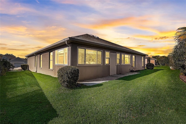 property exterior at dusk featuring a lawn and stucco siding