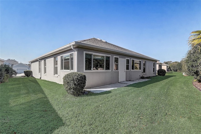 rear view of property featuring a shingled roof, a lawn, and stucco siding