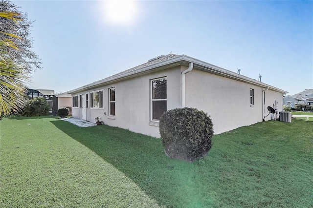 view of side of home featuring stucco siding, a lawn, and central air condition unit