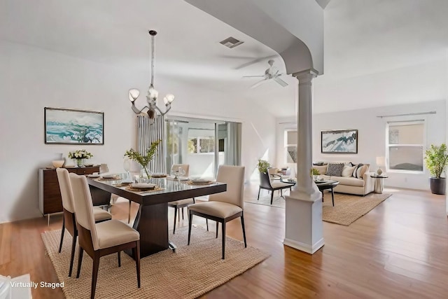 dining space featuring ceiling fan with notable chandelier, wood finished floors, visible vents, and ornate columns