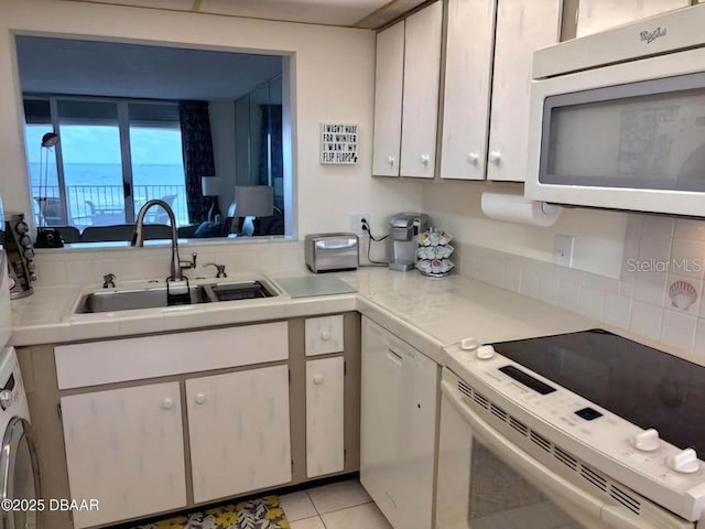 kitchen with light tile patterned floors, white appliances, a sink, white cabinets, and light countertops