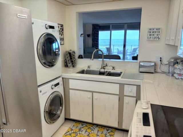 laundry area with stacked washer / dryer, laundry area, a sink, and light tile patterned floors