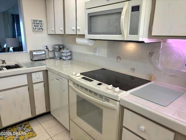 kitchen with light tile patterned floors, tile countertops, white appliances, a sink, and backsplash