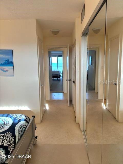 hallway with light tile patterned floors, visible vents, and light colored carpet