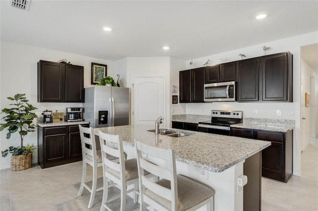 kitchen with dark brown cabinetry, a sink, visible vents, appliances with stainless steel finishes, and an island with sink