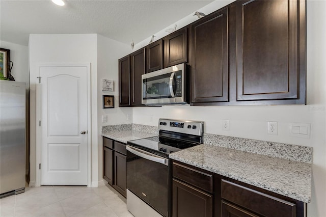 kitchen featuring dark brown cabinetry, light stone countertops, stainless steel appliances, a textured ceiling, and light tile patterned flooring