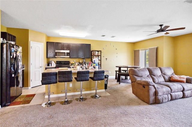 kitchen with a center island with sink, electric range oven, stainless steel microwave, light countertops, and black fridge