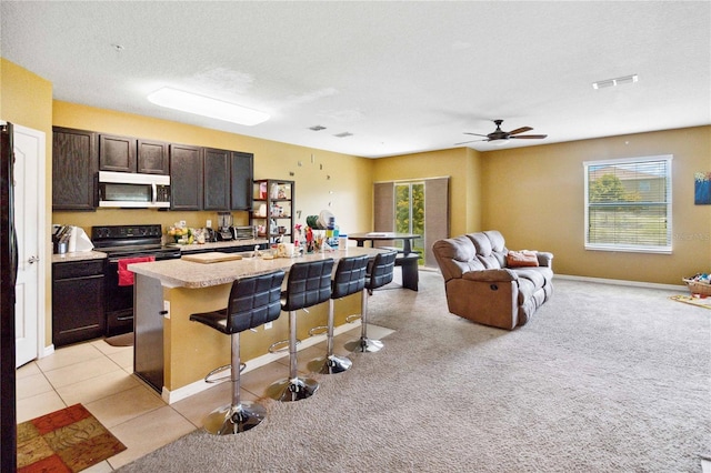 kitchen with stainless steel microwave, a kitchen breakfast bar, open floor plan, a kitchen island with sink, and black / electric stove