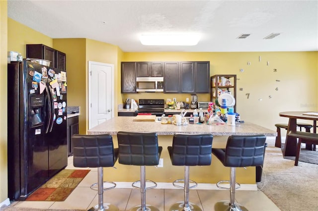 kitchen with black appliances, dark brown cabinets, an island with sink, and a kitchen bar