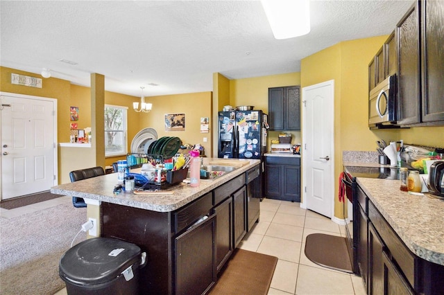 kitchen featuring range with electric stovetop, light countertops, stainless steel microwave, a center island with sink, and pendant lighting