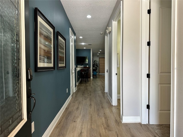 hall featuring light wood-type flooring, a textured ceiling, baseboards, and recessed lighting