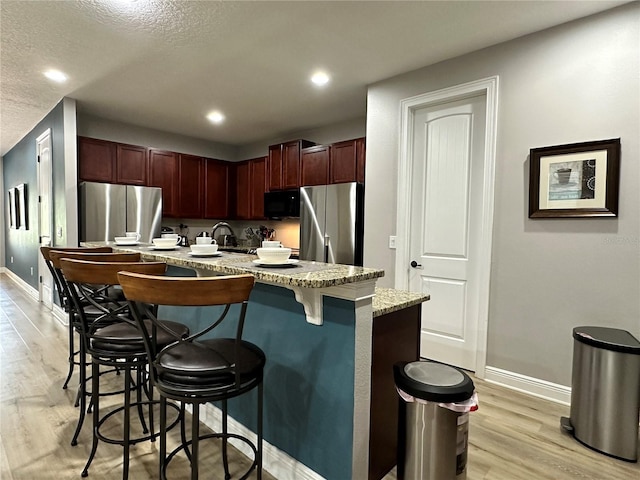 kitchen featuring black microwave, light wood-style flooring, a breakfast bar, and freestanding refrigerator