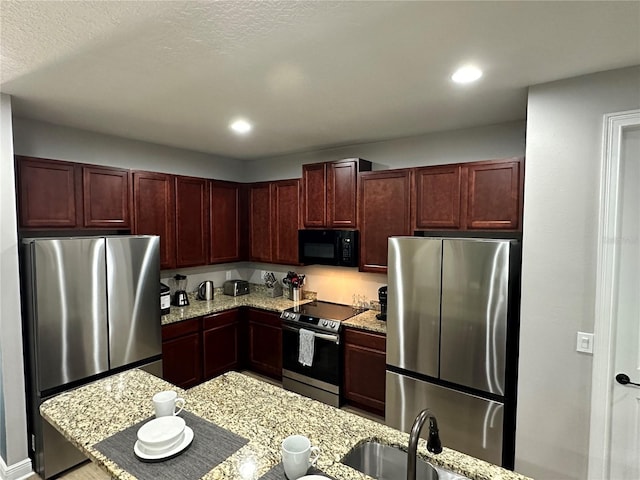 kitchen with reddish brown cabinets, stainless steel appliances, light stone counters, and a sink