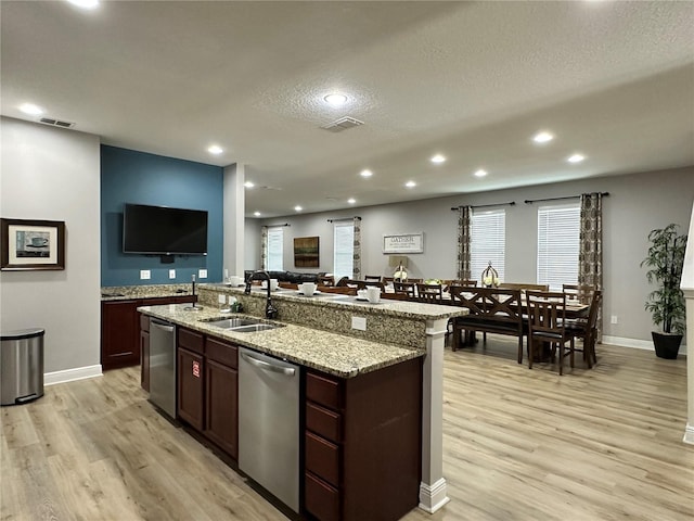 kitchen featuring a sink, light wood finished floors, open floor plan, and stainless steel dishwasher