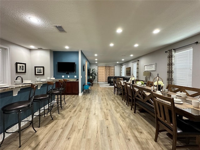 dining space featuring light wood-style flooring, visible vents, a textured ceiling, and recessed lighting