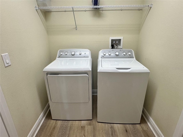 washroom featuring washing machine and dryer, laundry area, baseboards, and wood finished floors