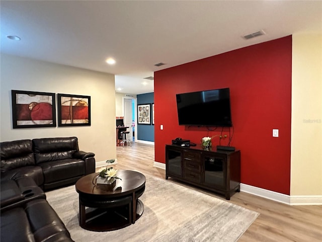 living room with an accent wall, wood finished floors, visible vents, and baseboards