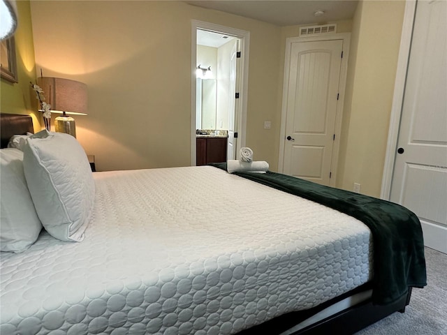 carpeted bedroom featuring ensuite bath and visible vents