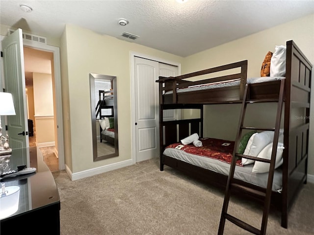 bedroom with carpet floors, a closet, visible vents, a textured ceiling, and baseboards