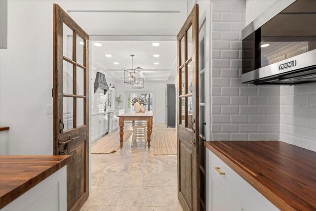 kitchen featuring butcher block countertops, backsplash, white cabinetry, stainless steel appliances, and custom exhaust hood