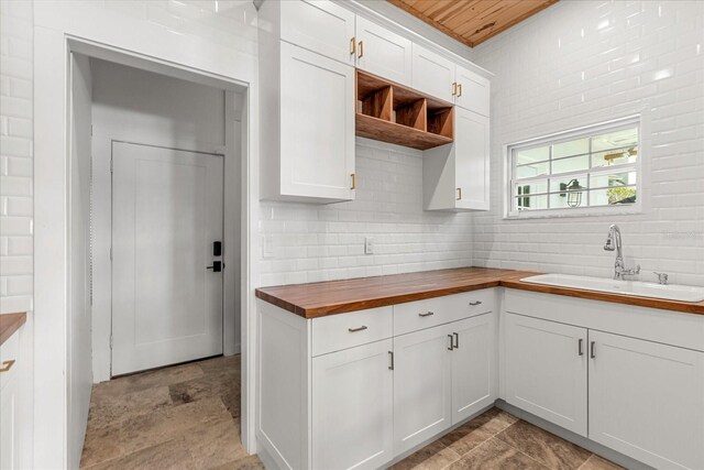 kitchen with a sink, butcher block counters, decorative backsplash, white cabinetry, and open shelves