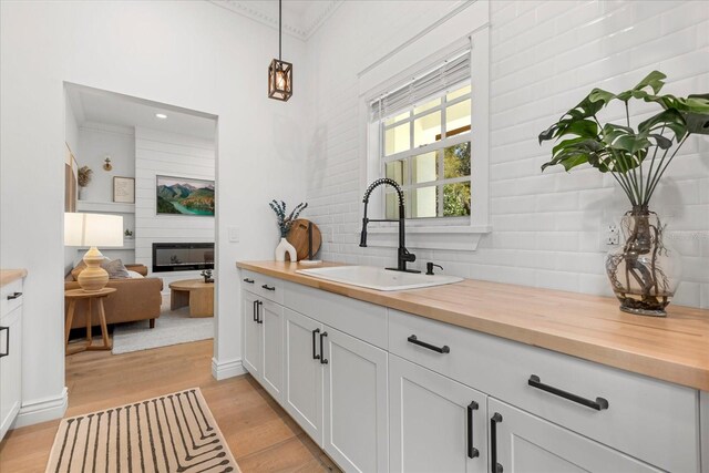 kitchen featuring backsplash, wooden counters, decorative light fixtures, light wood-style floors, and a sink