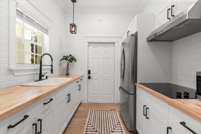 kitchen with a sink, under cabinet range hood, freestanding refrigerator, and butcher block countertops