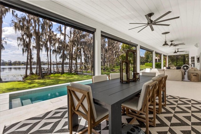 view of patio / terrace with outdoor dining area, a ceiling fan, an outdoor pool, and a water view