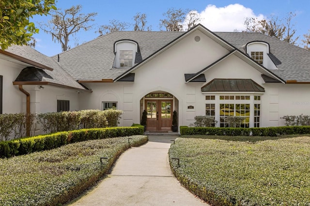 french country home with a shingled roof, metal roof, french doors, and stucco siding