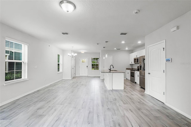 kitchen featuring light wood-style flooring, a sink, white cabinets, open floor plan, and appliances with stainless steel finishes