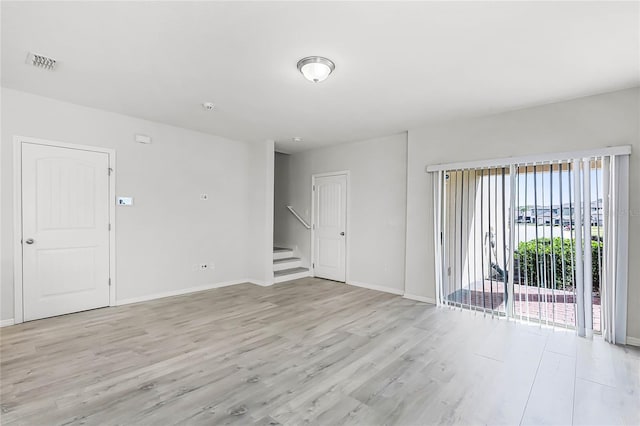 empty room with light wood finished floors, baseboards, stairway, and visible vents