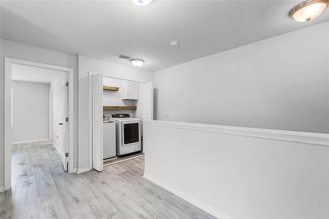 kitchen featuring light wood finished floors, visible vents, white cabinets, baseboards, and washing machine and dryer