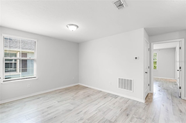 empty room with light wood-type flooring, baseboards, and visible vents