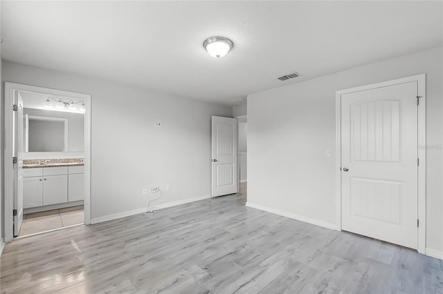 unfurnished bedroom with light wood-type flooring, ensuite bath, visible vents, and baseboards