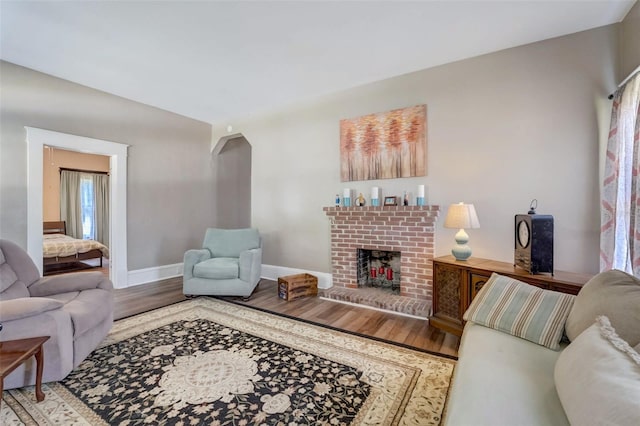 living room with arched walkways, a fireplace, wood finished floors, and baseboards