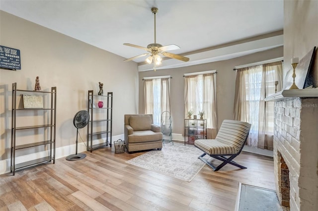 living area with light wood-type flooring, ceiling fan, a fireplace, and baseboards