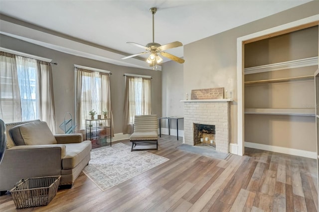 living area with built in shelves, a fireplace, wood finished floors, a ceiling fan, and baseboards