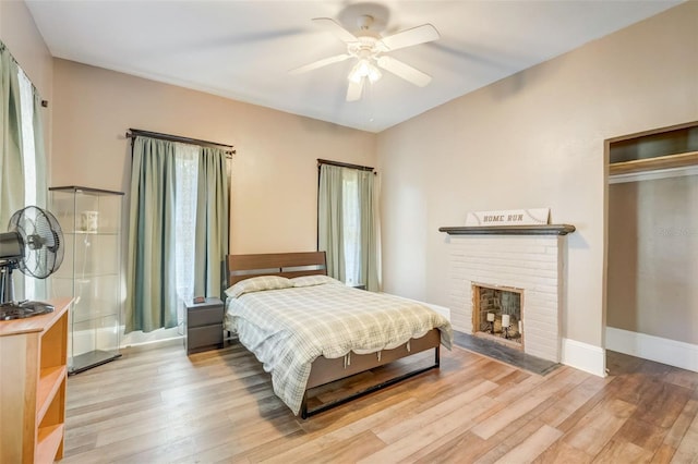 bedroom with a brick fireplace, wood finished floors, a ceiling fan, and baseboards