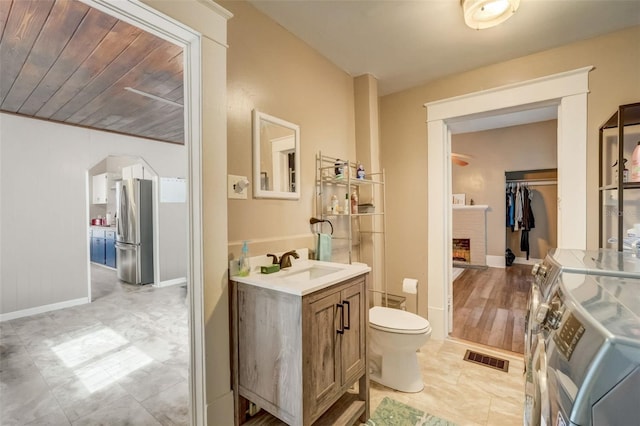 bathroom with baseboards, visible vents, toilet, vanity, and a fireplace