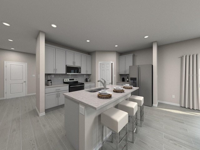 kitchen with a center island with sink, appliances with stainless steel finishes, a kitchen breakfast bar, a sink, and backsplash