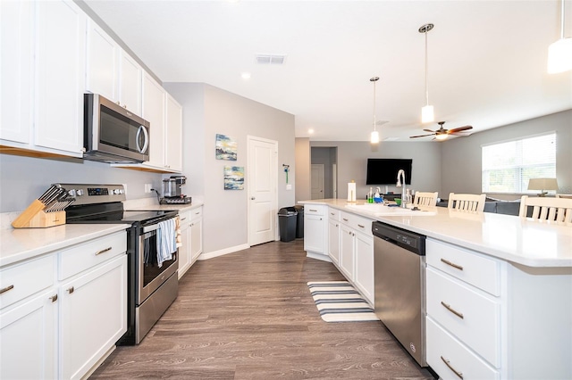 kitchen with dark wood-style flooring, pendant lighting, stainless steel appliances, light countertops, and white cabinetry