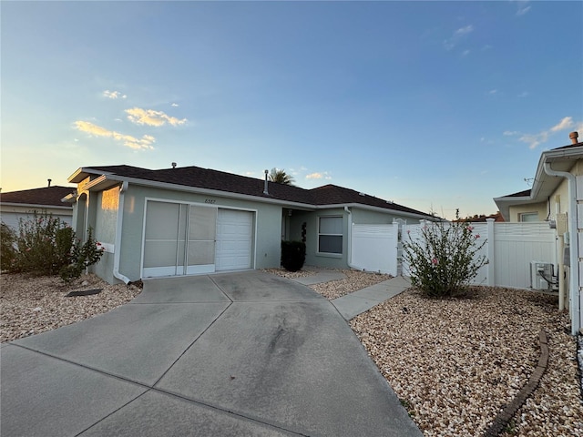 ranch-style home with driveway, a garage, fence, and stucco siding