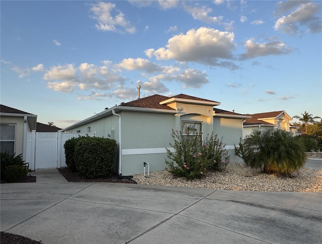 view of home's exterior with a shingled roof, fence, and stucco siding