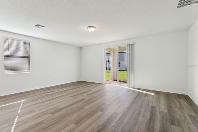 unfurnished room featuring baseboards, visible vents, wood finished floors, and a textured ceiling