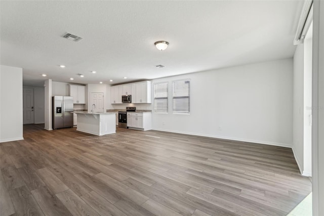 unfurnished living room featuring recessed lighting, baseboards, a textured ceiling, light wood-style floors, and visible vents