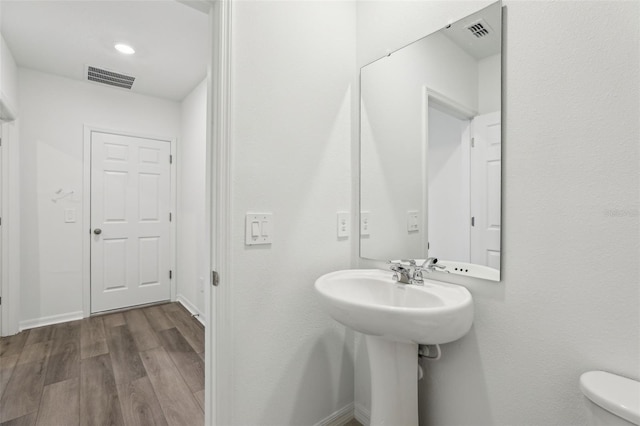half bathroom with baseboards, visible vents, toilet, and wood finished floors