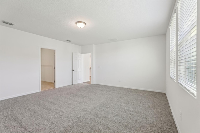 unfurnished room featuring light carpet, baseboards, visible vents, and a textured ceiling
