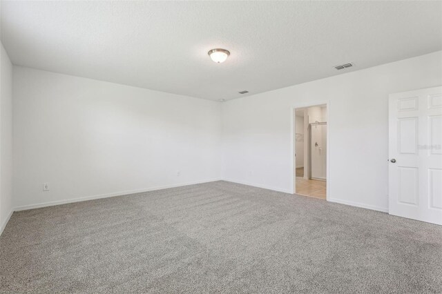 unfurnished room with light carpet, a textured ceiling, baseboards, and visible vents